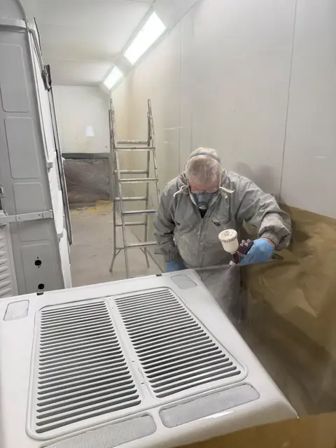 Mark in a mask and overalls spraying a white van panel with a spray gun in RPM Autocare's spray booth